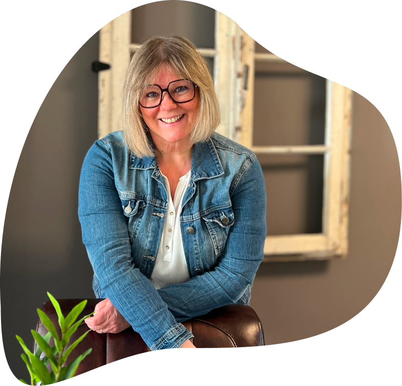 Maren Dondit, lächelnd in Jeansjacke, auf einem braunen Ledersessel vor einem Fensterrahmen